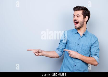 Portrait of young stylish guy in jeans shirt, pointing on copyspace. He is surprised and very excited Stock Photo