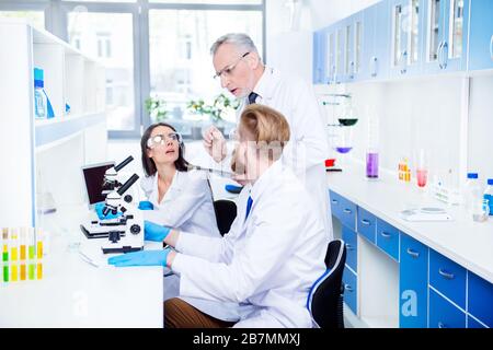 Teamwork and teambuilding concept. A group of three scientists in labcoats are discussing their researches in the bright lab Stock Photo