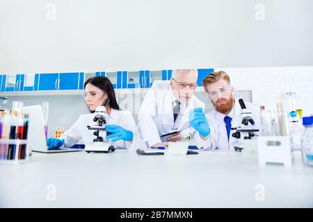 Science and teamwork concept - a group of three scientists are making research in clinical laboratory in labcoats. Cropped photo Stock Photo