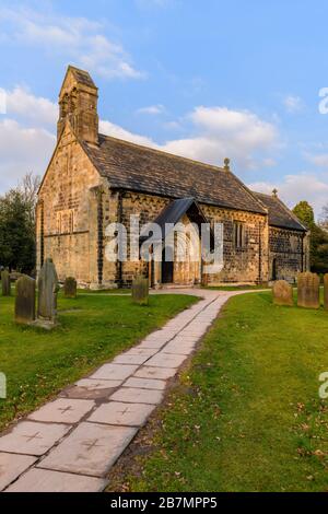 Exterior of historic Church of St John the Baptist, churchyard memorials & pathway leading to carved Norman doorway arch - Adel, Yorkshire, England UK Stock Photo