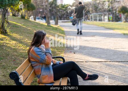 Couple breaking up a relation in a park while woman sitting and crying on bench and man leaving her in park. Stock Photo