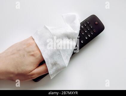 Close up view of man hand using antibacterial wet wipe for disinfecting home TV remote control. Stock Photo
