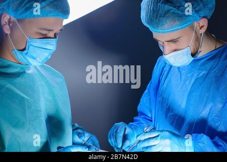 close-up portrait of two surgeons operating in an operating room with instruments. In sterile medical surgical special clothing and masks. Surgery of Stock Photo