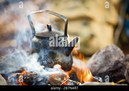 Man and woman making coffee in big kettle on campfire in forest on shore of lake, making a fire, grilling. Happy couple exploring Finland. Scandinavia Stock Photo