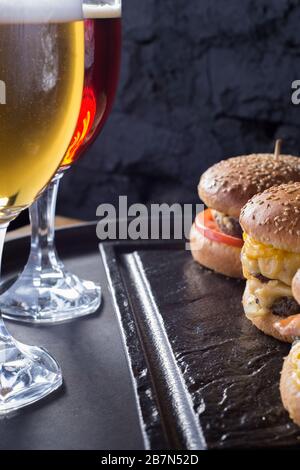 mug of beer with hamburger and fries close-up, beer glasses with craft dark and light beer with foam, against a background of burgers, with a variety Stock Photo