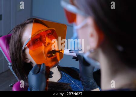 Portrait of a dentist doctor performing the procedure of professional teeth whitening using ultraviolet radiation. Patient and doctor in protective or Stock Photo