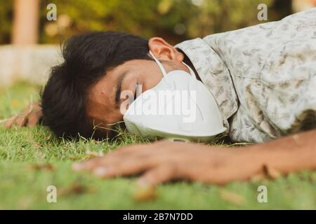 Sick young man fell down on ground with medical face mask - concept showing of sick, dizzy , ill health, dehydration or sun stroke. Stock Photo