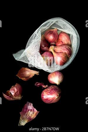 Red onions in mesh bag and some on floor isolated on black background Stock Photo