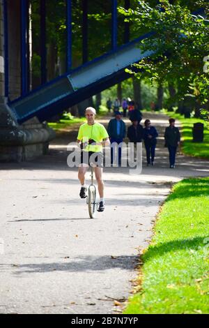 Male unicyclist dressed in a bright yellow top cycling beside the River Severn in the Quarry Park in Shrewsbury. Stock Photo