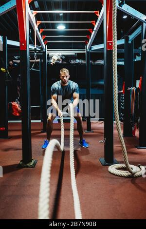 Happy fit men with battle ropes exercise in the fitness gym Stock Photo