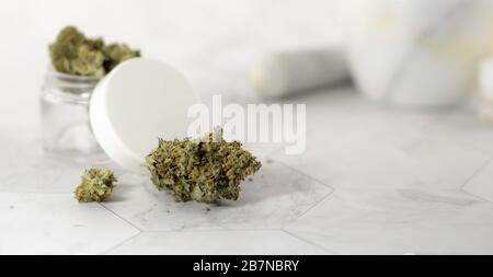 Concept of new organic skin care cosmetic. Cream container with medical marihuana bud on a white marble surface Stock Photo