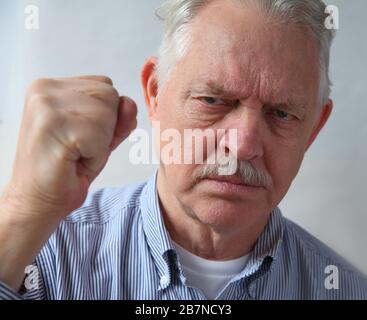 Older man holds his fist up in anger Stock Photo