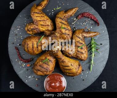 grilled chicken legs and wings with red sauce on a black stone surface Stock Photo
