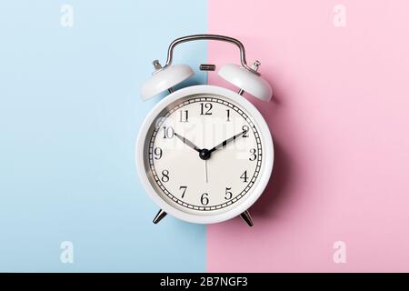 White vintage alarm clock on blue and pink background. Time concept Stock Photo