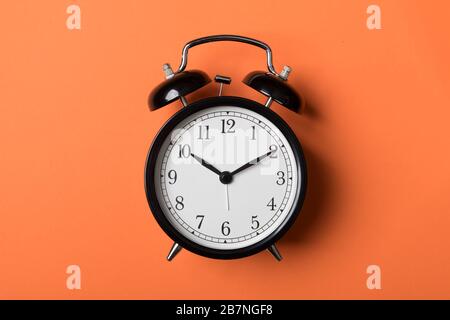 Black vintage alarm clock on orange background. Time concept Stock Photo