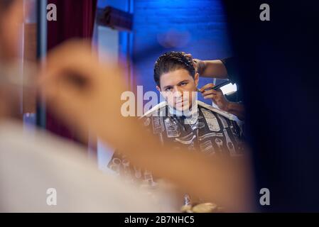 Master cuts hair and beard of men in the barbershop, hairdresser makes hairstyle for a young man Stock Photo