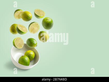 limes flying in white bowl on green background with space for copy Stock Photo