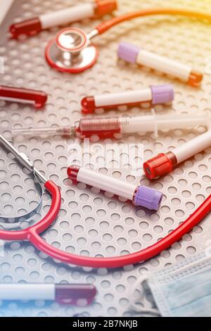 Blood sample along with syringe, protective mask and stethoscope on metal surface Stock Photo