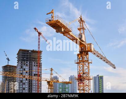 several construction tower cranes of different heights at a building site during the construction of blocks of flats, view against the sky Stock Photo