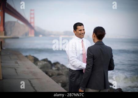 Laughing businessman having a conversation with a colleague while standing at the edge of a waterfront overlooking a harbor. Stock Photo