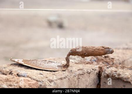 Trowel on wall on the unfinished home made from raw clay brick, made on local brick factory, horizontal, side view Stock Photo