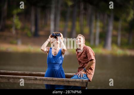 Happy mature couple having fun bird watching together at the lake. Stock Photo