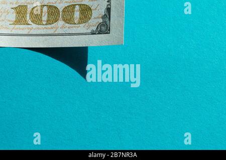 Piece of 100 dollar bill at the upper-left corner on the bright blue background. Conceptual photo, minimalistic design Stock Photo