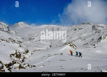 Walkers hiking through the snow below the Langdale Pikes and Sergeant Man in Langdale, Lake District national park, Cumbria Stock Photo