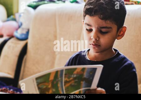 A little schoolboy doing homework. Reading book. Authentic view of a young kid in a cozy home environment Stock Photo
