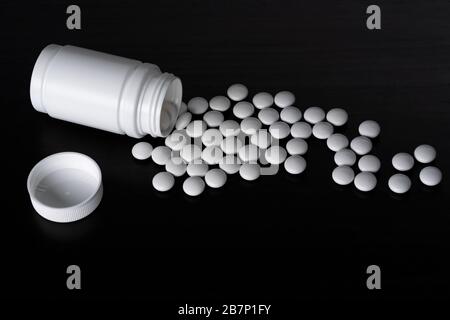 A black background, a white jar lying on its side next to the lid and white round tablets, the view from the side Stock Photo