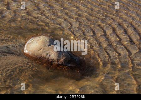Rock being hit by water and forming ripples Stock Photo