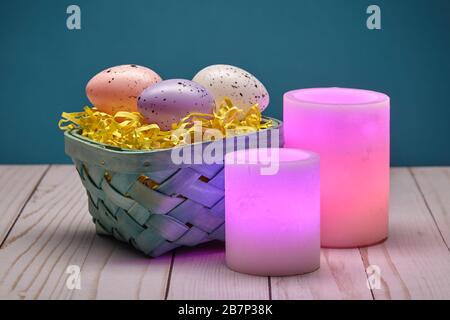 Two Glowing Pink Wax Candles and a Basket of Easter Eggs Stock Photo
