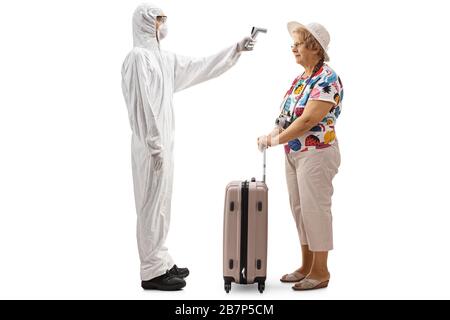 Full length profile shot of a man wearing a white protective suit and measuring temperature of an elderly woman with a suitcase isolated on white back Stock Photo