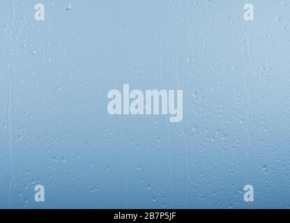 Close up raindrops and water runs on glass window pane surface over grey and blue sky background on rainy day Stock Photo