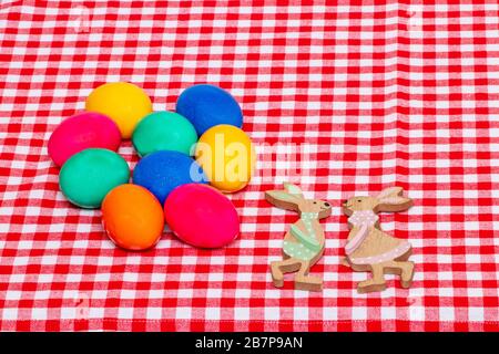 Happy Easter greeting card template. Top view of colorful eggs  and two wooden bunnies on a red checkered tablecloth. Large space for text. Religion a Stock Photo
