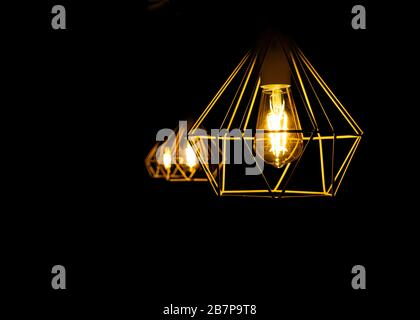 Modern metal lampshade with a yellow led lamp isolated on a black background. Abstract interior fragment. Selective focus. Stock Photo