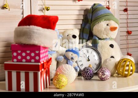 Christmas decorations in festive room. Snowmen, teddy bears, Christmas balls and present boxes near alarm clock. Toys placed on wooden wall background. Celebration and New Year decor concept Stock Photo