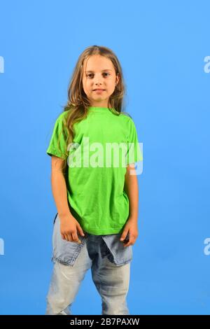 Child looks like hip hop star wearing casual clothes. Childhood and lifestyle concept. Kid poses as Bgirl in cool style. Girl with smiling face on blue background. Stock Photo