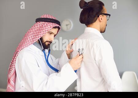 Arab doctor male listens in a stethoscope to a patient in a clinic office Stock Photo