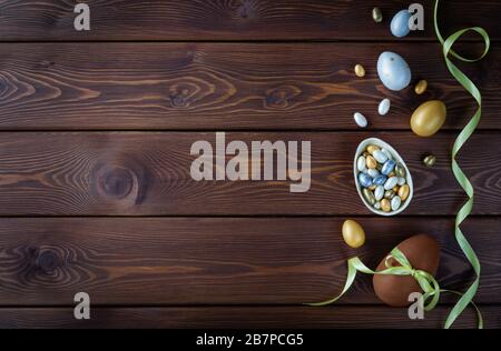 Chocolate and colored Easter eggs with color ribbon bows on wooden background. Happy Easter card. Stock Photo