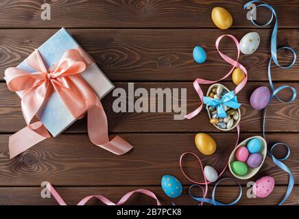 Happy Easter card. Gift box with Easter eggs. Chocolate and colored Easter eggs with color ribbon bows on wooden background. Stock Photo
