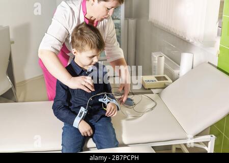 A nurse attaches electrodes to the boy to remove the cardiogram. Electrocardiography - a method of registration and study of electrical fields generat Stock Photo