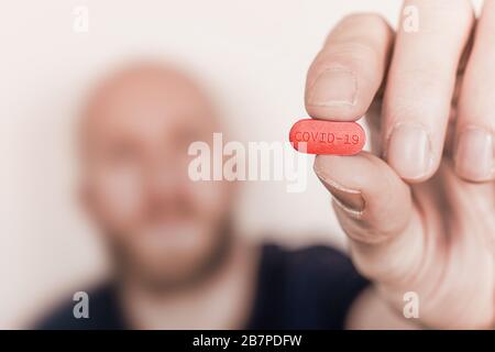 Illustration of a cure for Coronavirus Covid-19, man holding a pill with Covid-19 label. Stock Photo