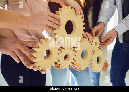 Hands of people hold wooden gears indoors. Stock Photo