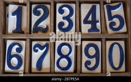Blue and white ceramic tiles with raised numbers 0 to 9 arranged in two rows in wooden box. Stock Photo
