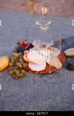 Top view of wooden board with pieces of bread pear figs nuts green grape and delicious cheese with white wine on blanket Stock Photo