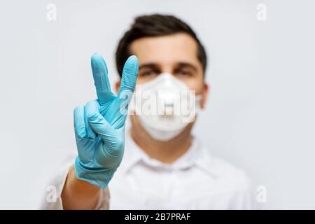 Portrait of doctor in medical uniform with a protective face mask and a gloved hand making a victory sign. Stop COVID-19 concept. Stock Photo