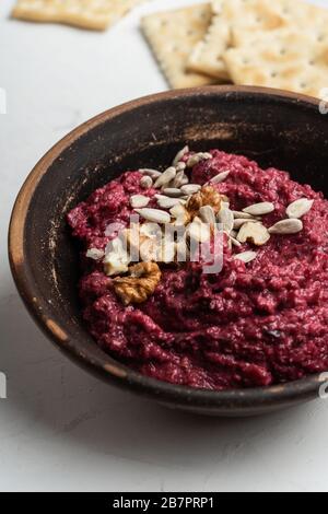 Healthy snack, gourmet dip. Beetroot hummus with walnuts sunflower seeds on top in ceramic bowl, close up Stock Photo