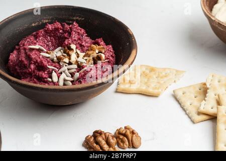 Healthy snack, gourmet dip. Beetroot hummus with walnuts sunflower seeds on top in ceramic bowl, close up Stock Photo