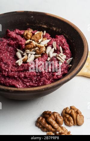 Healthy snack, gourmet dip. Beetroot hummus with walnuts sunflower seeds on top in ceramic bowl, close up Stock Photo